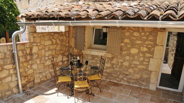 A stone patio with a tiled roof, a table with chairs, and a window with shutters. - Au Mazet de Carmélina, an old building dating from 1850 in the heart of the Alpilles mountains (Paradou)