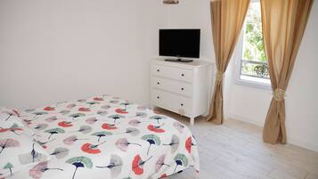 Un dormitorio con cama, televisor sobre una cómoda y ventana con cortinas.