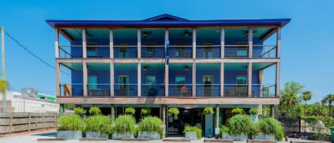Un edificio de varios pisos con balcones, ventanas amplias y plantas en macetas al frente.