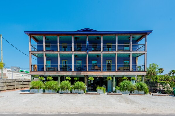 A multi-story building with balconies, large windows, and potted plants in front.