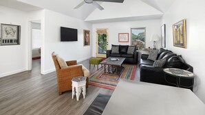 A spacious living room with a ceiling fan, a black leather sofa, a wooden coffee table, and a colorful rug.