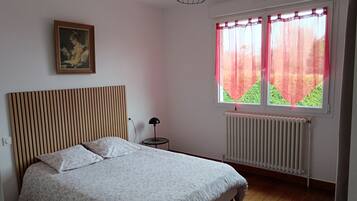 Een slaapkamer met een bed, een radiator, een raam met gordijnen, een lamp en een schilderij aan de muur.