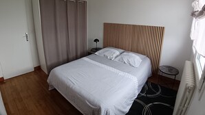 A bedroom with a bed, a curtain, a lamp, a radiator, and a window.
