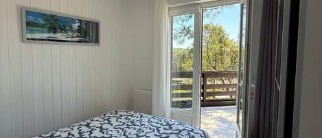 Une chambre à coucher comprenant un lit, un ventilateur de plafond, un tableau et une porte-fenêtre coulissante donnant sur un espace extérieur.