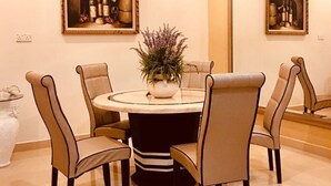 Un comedor con una mesa redonda, cuatro sillas, una araña y dos cuadros en las paredes.