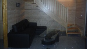 A wooden interior with a staircase, a black sofa, and a glass coffee table.