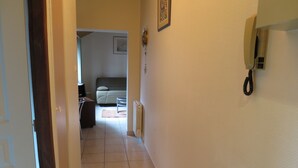 Un pasillo que conduce a un dormitorio con cama, mesita de noche y teléfono instalado en la pared.