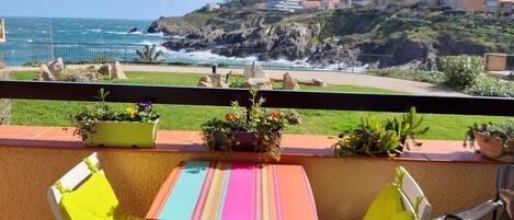 Un balcón con mesa y sillas, con vista a una costa rocosa y olas rompiendo contra la orilla.