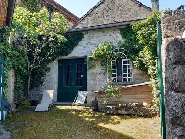 A stone building with a green door and window, surrounded by greenery and a grassy yard.