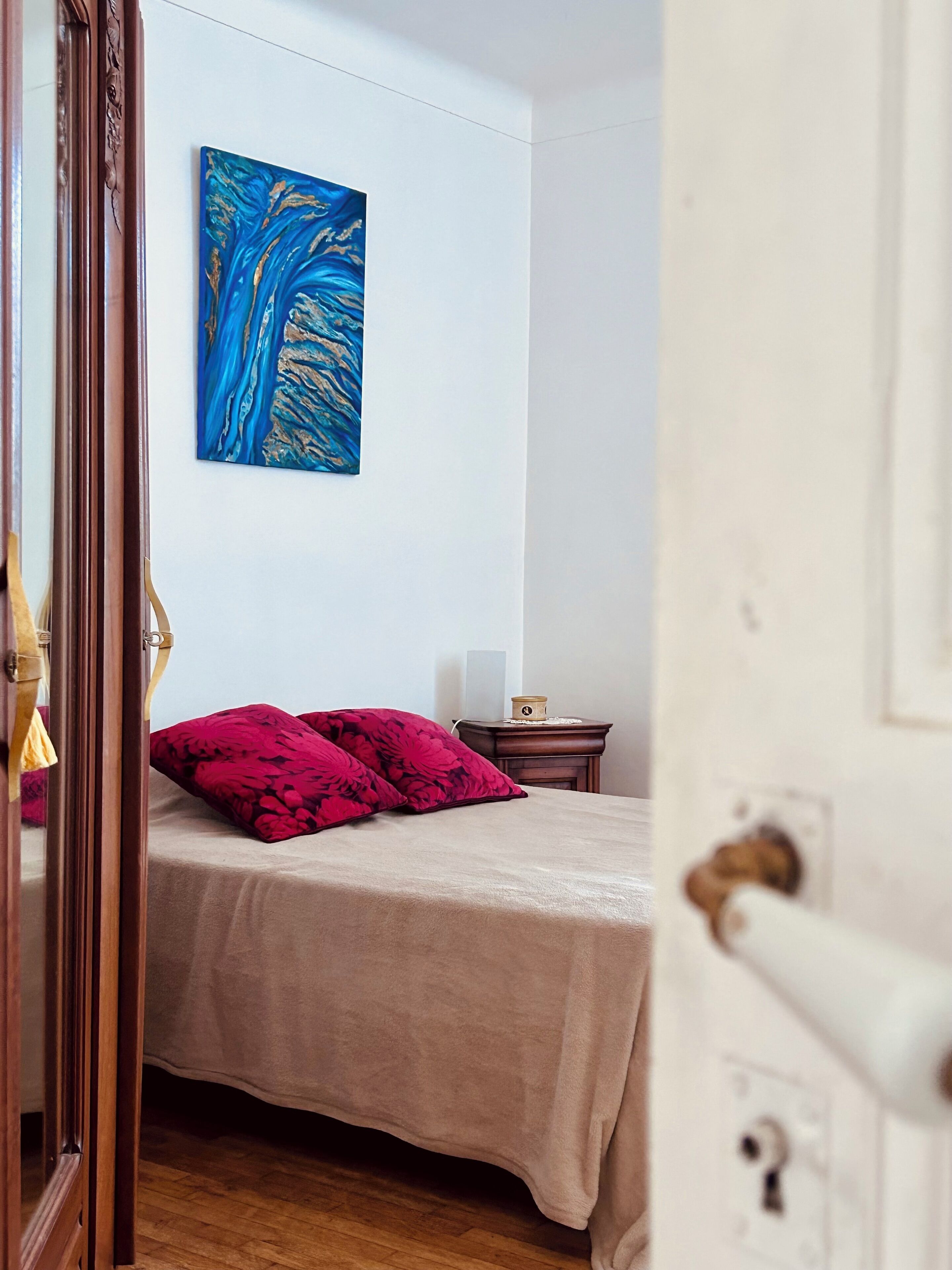 Ein Schlafzimmer mit einem Bett, einem Nachttisch, einem Wandbild und einer Holztür.