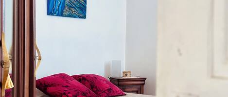 Ein Schlafzimmer mit einem Bett, einem Nachttisch, einem Wandbild und einer Holztür.