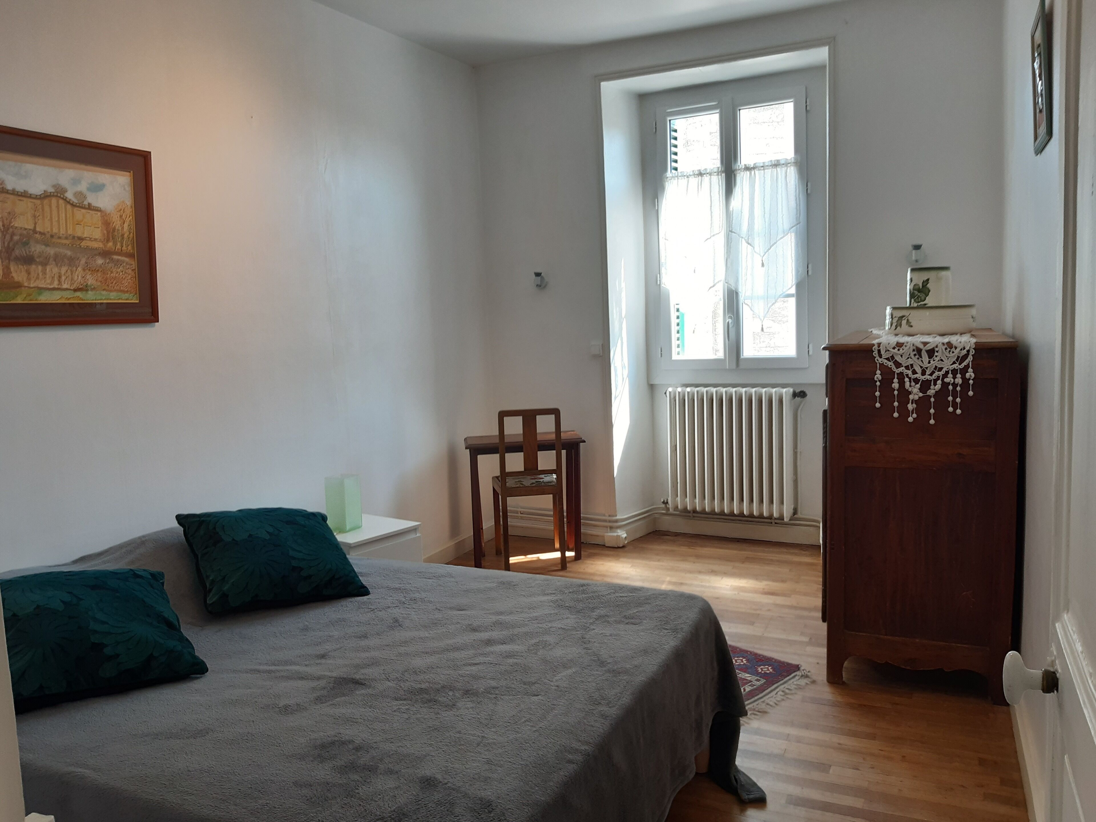 Een slaapkamer met een bed, een stoel, een radiator en een raam.
