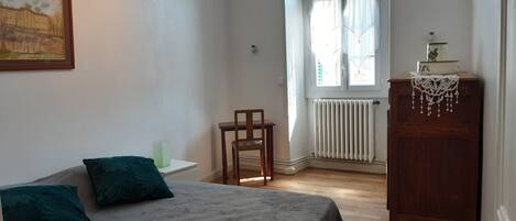 A bedroom with a bed, a chair, a radiator, and a window.