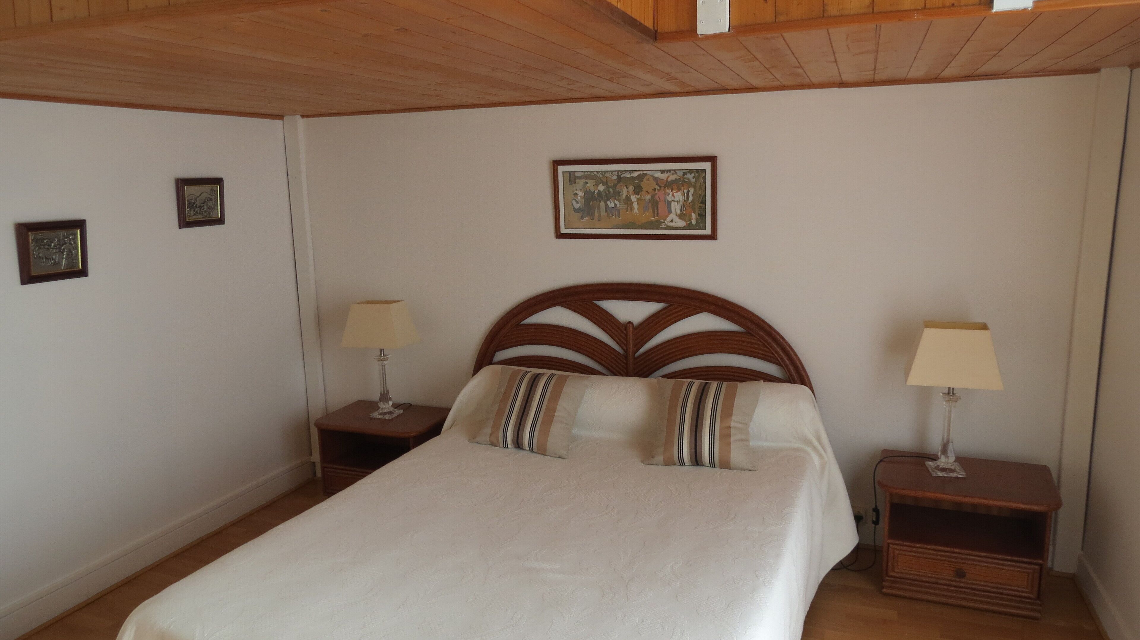 Une chambre à coucher avec une tête de lit en bois, deux tables de chevet avec des lampes, un lit avec des oreillers à rayures et un tableau encadré au mur.