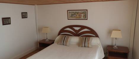 Une chambre à coucher avec une tête de lit en bois, deux tables de chevet avec des lampes, un lit avec des oreillers à rayures et un tableau encadré au mur.