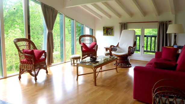 Un salon spacieux avec de grandes fenêtres, des meubles en osier et un canapé rouge.