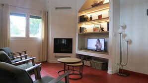 Un salon comprenant un téléviseur, une bibliothèque, un coin repas et une fenêtre avec des rideaux.
