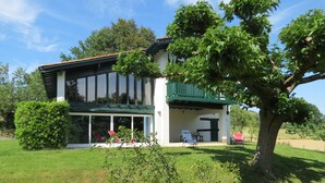 Une maison moderne à deux étages, dotée d’un patio couvert, de grandes fenêtres et d’une pelouse bien entretenue.