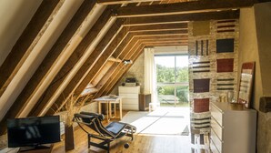Une chambre de style loft moderne avec un plafond en pente, des poutres en bois, une grande fenêtre, un téléviseur à écran plat, un fauteuil confortable et une petite kitchenette.