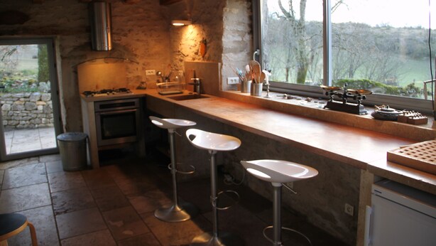 Une cuisine avec un mur en pierre, une grande fenêtre et un coin bar avec des tabourets.