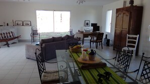Un vaste espace de vie comprenant un canapé, une table à manger et des chaises. On aperçoit un meuble en bois et un téléviseur au fond.