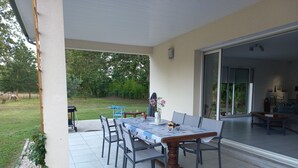 Une terrasse extérieure avec une table dressée pour le repas, entourée de chaises, et donnant sur un jardin.