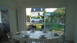 A dining area with a table set for four, chairs, and a view of a parked car and house through a glass door.