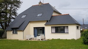 A two-story house with a sloped roof, a front door, and a small patio with two white chairs.