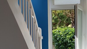 A staircase with white railings leading to a glass door, a blue wall, and a green hedge outside.