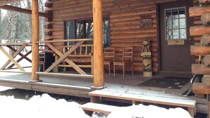 Une cabane rustique en rondins de bois, dotée d’un porche en bois, d’une pancarte d’accueil et d’une autre sur laquelle on peut lire : « Allez les Broncos ! ».