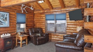 L’intérieur d’une cabane en rondins, avec une cheminée, des canapés en cuir, un téléviseur et une décoration faite de bois de cerf.