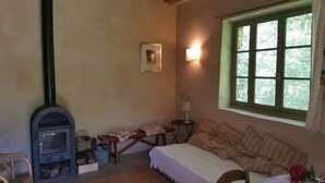Een knus interieur met een open haard, een bed, een raam met uitzicht op bomen en een kleine tafel met een lamp.