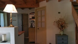 Een kamer met een houten plafond, een lamp, een deur, een vaas met gedroogde bloemen en een blauwe kapstok.