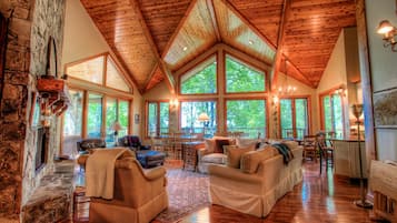 Un vaste salon doté d’un haut plafond en bois, de grandes fenêtres et d’une cheminée en pierre.