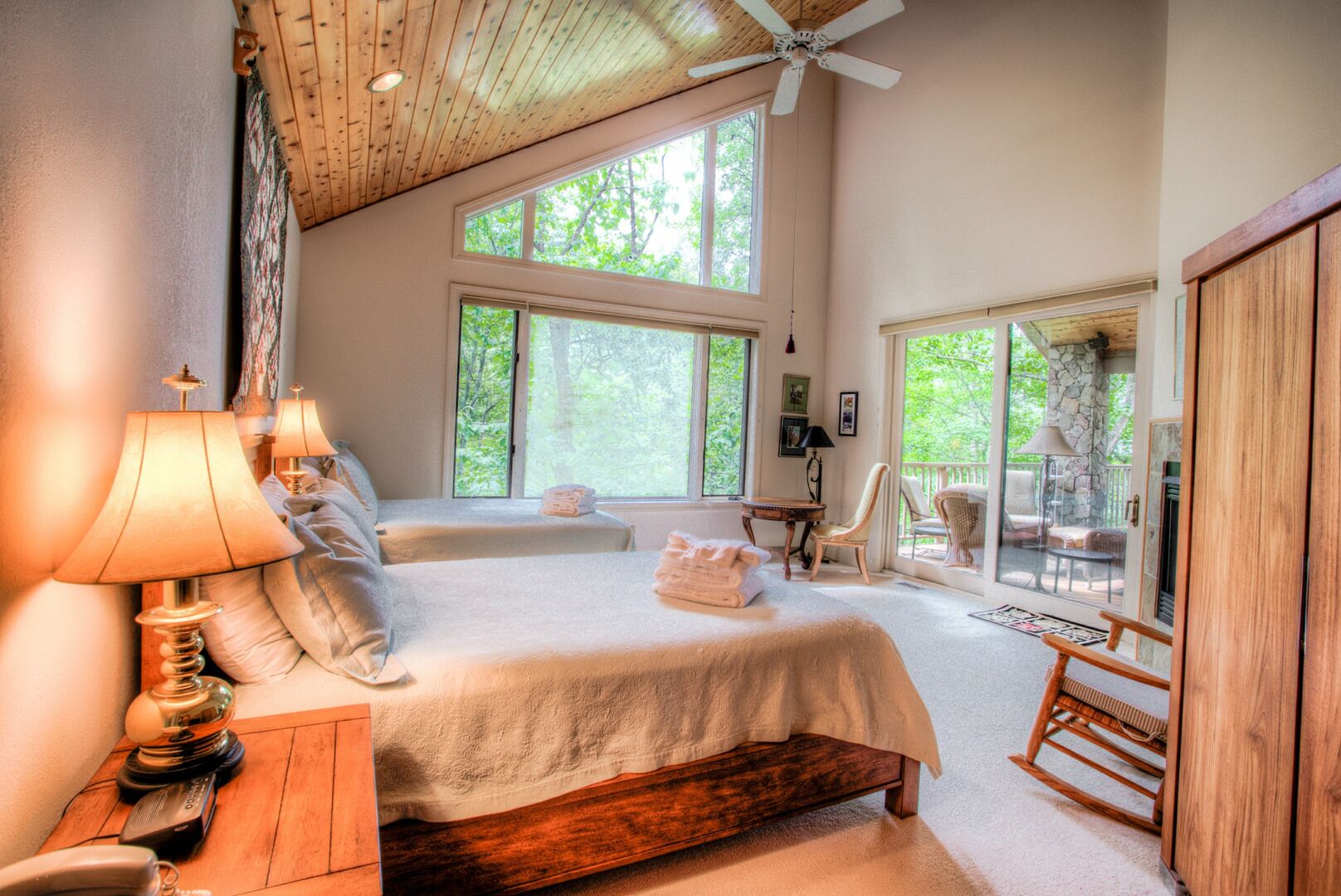 A bedroom with two beds, large windows, a ceiling fan, and a view of the outdoors.