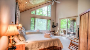 A bedroom with two beds, large windows, a ceiling fan, and a view of the outdoors.