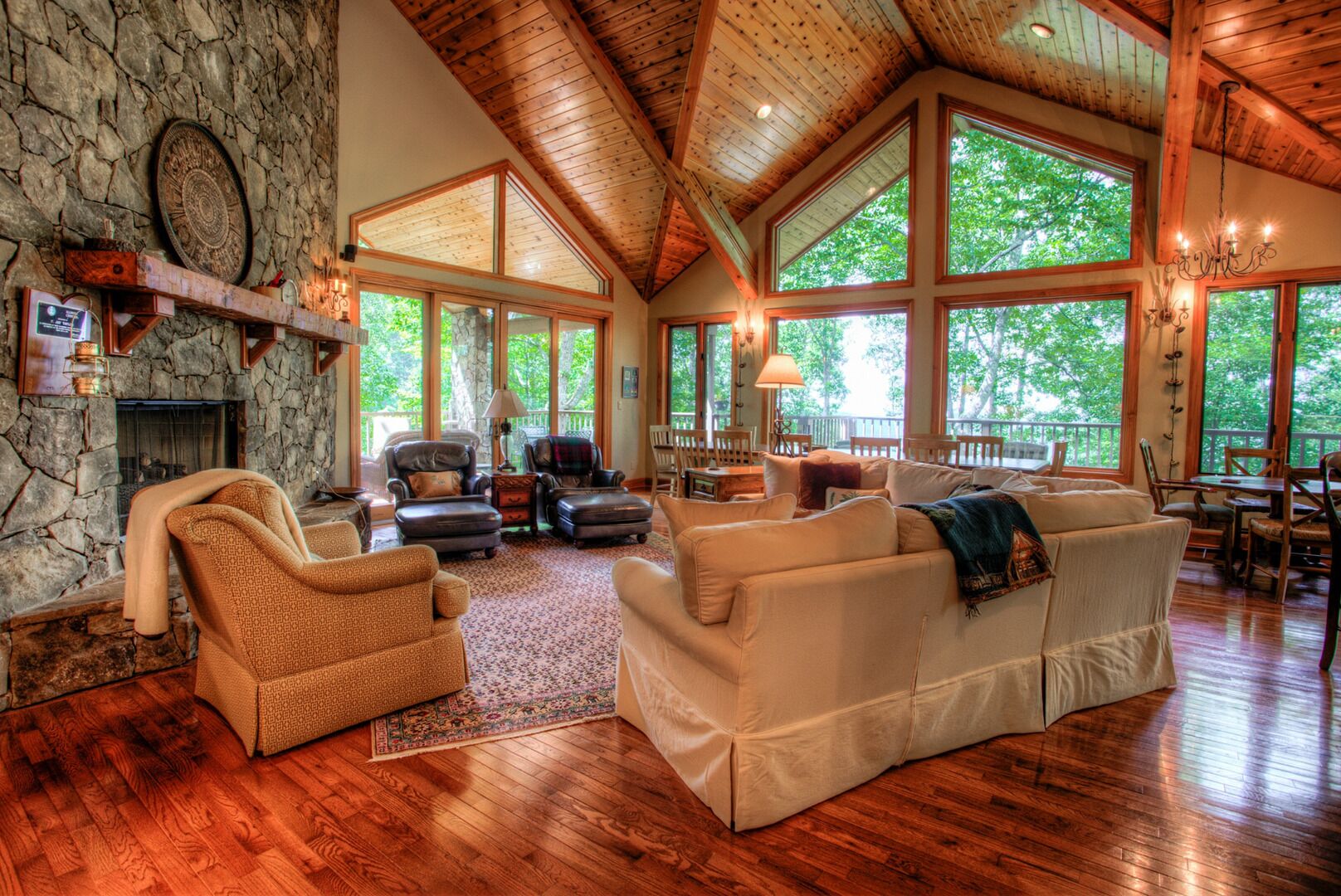 Un salon spacieux doté d’une cheminée en pierre, de grandes fenêtres et d’un plancher en bois.