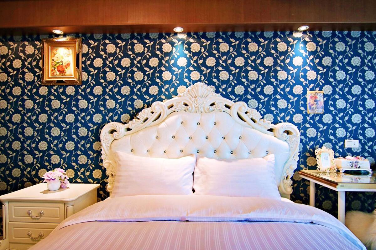Un dormitorio con cabecera capitonada, una mesita de noche con un florero y un aparador.