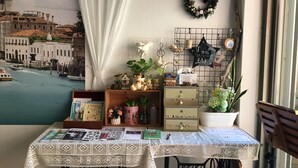 Una habitación con vistas a un paisaje urbano, una mesa con mantel de encaje y varios objetos decorativos, incluyendo un letrero con forma de estrella, una guirnalda y un cofre de madera.