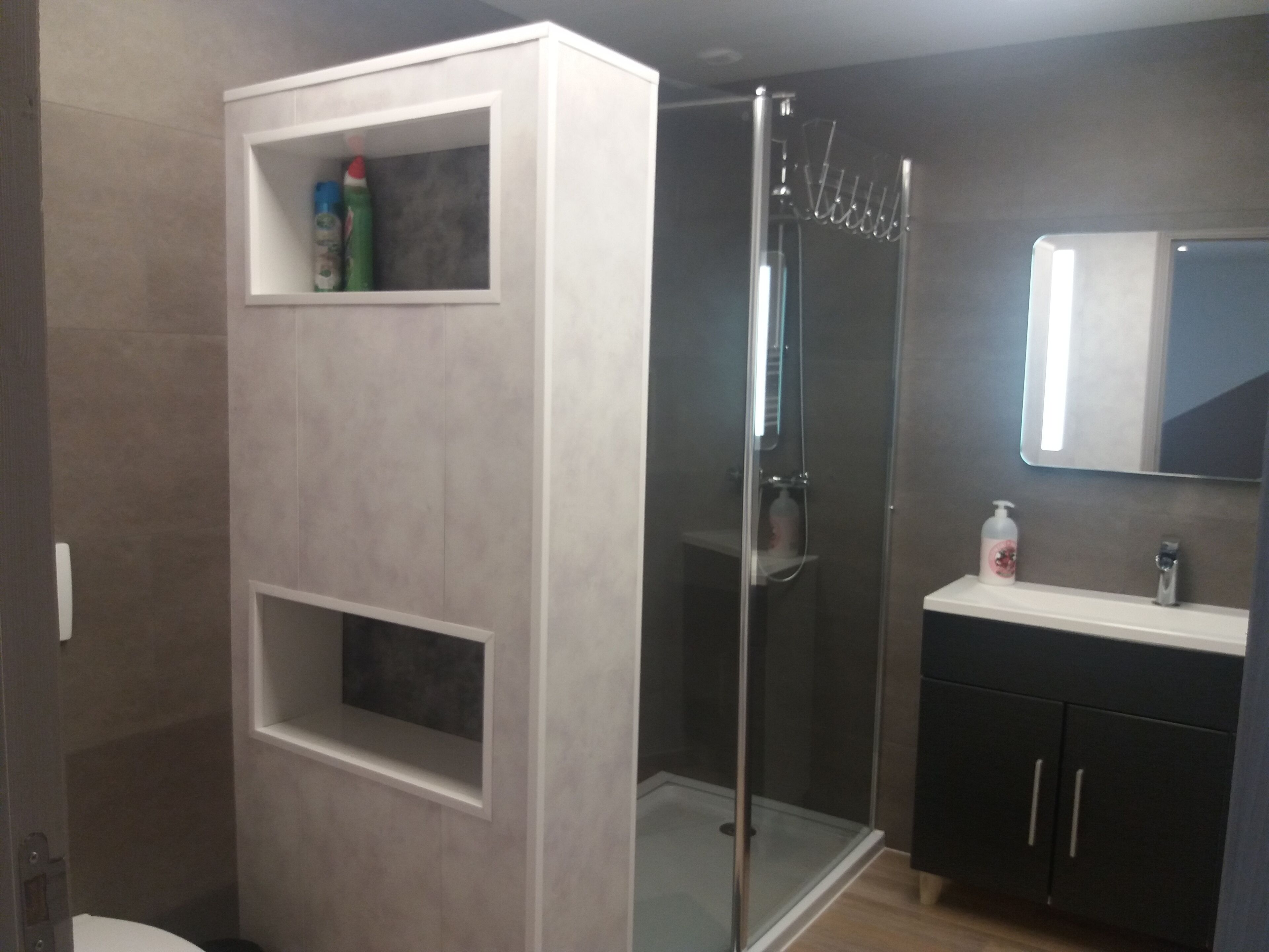 A modern bathroom with a glass shower enclosure, a white vanity with a mirror, and built-in shelves with toiletries.
