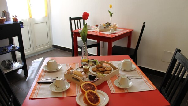 A breakfast table set with cups, plates, a vase with a flower, and a tray of pastries. - B&b Scirocco d'Africa (Catania)