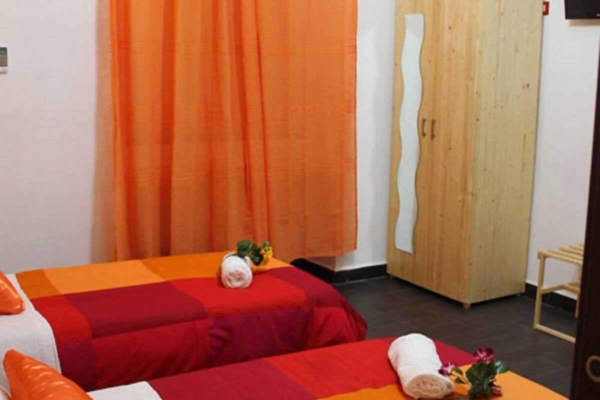 Ein Zimmer mit zwei Betten, orangefarbenen Vorhängen, einem Holzschrank und einem kleinen Tisch.