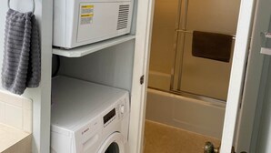 Una sala de bugaderia amb rentadores apilades i una dutxa visible per una porta oberta.