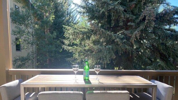 Una terrassa de fusta amb taula i dues cadires, amb vista a un bosc dens.