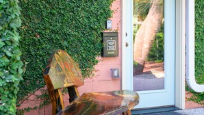 A wooden bench with a carved backrest and seat, positioned on a concrete surface in front of a door with a glass panel.
