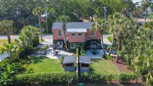 A two-story house with a patio area, surrounded by lush greenery and palm trees.