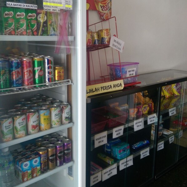 A refrigerated display case with various food items and beverages, including cans of Milo, 7up, and Red Bull, as well as shelves stocked with Nescafe and other products. - Daddy's Inn (Lumut)