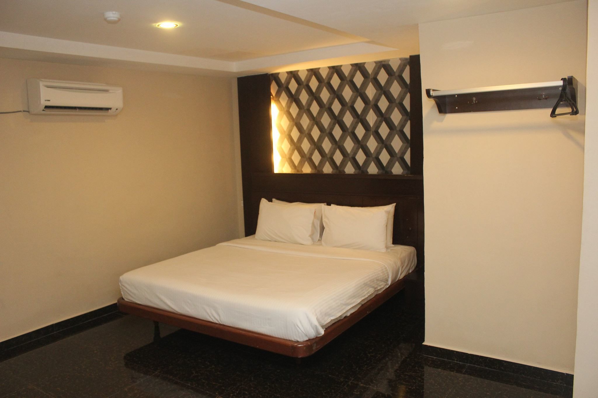 Une chambre d’hôtel avec un lit, un climatiseur fixé au mur, une décoration murale à motifs et une étagère avec un luminaire.