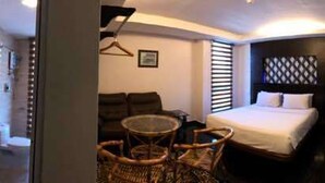 A hotel room with a bed, a small table, a chair, a TV, and a control panel on the wall. - Daddy's Inn (Lumut)