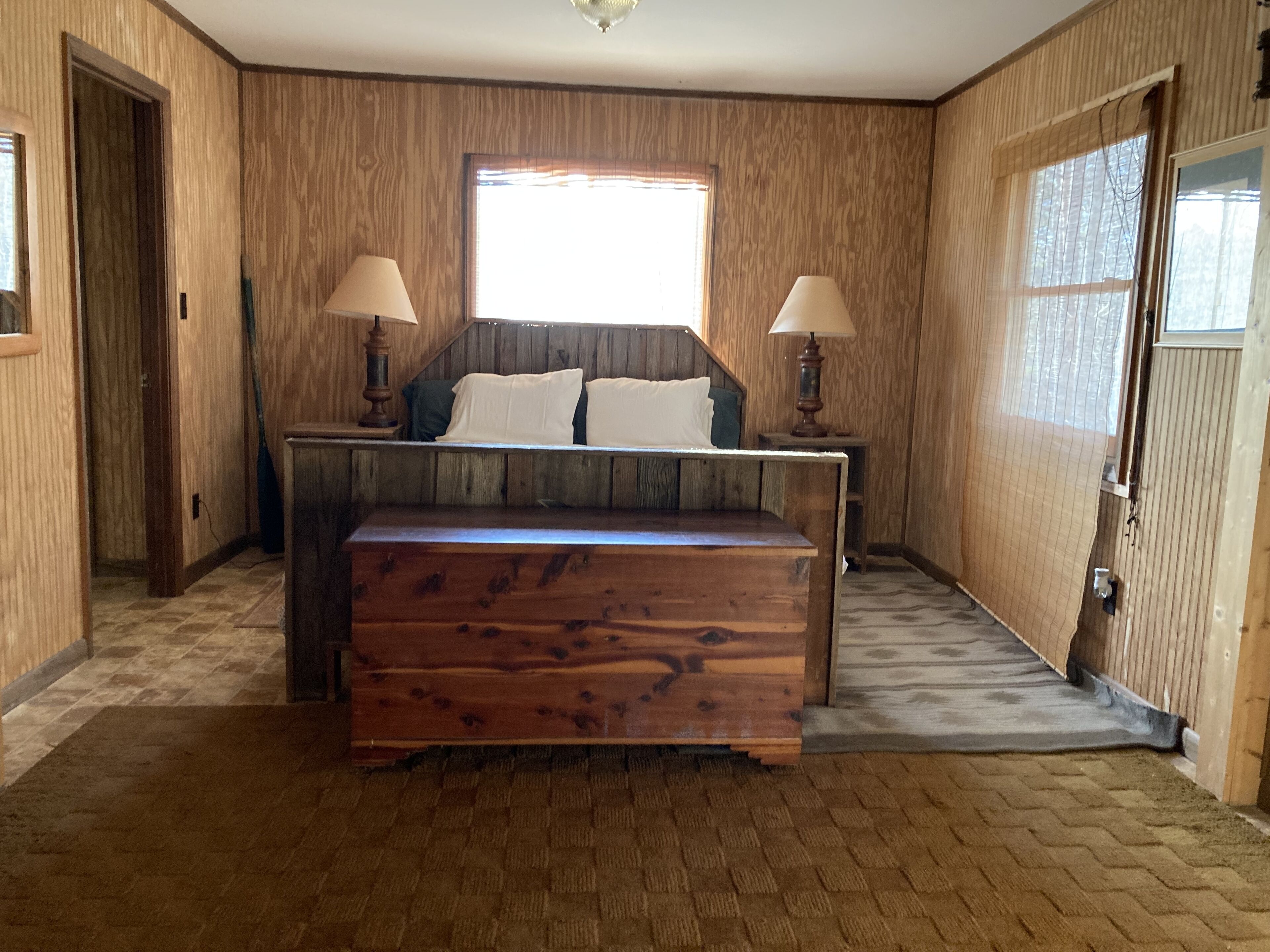 Un dormitorio con paneles de madera, una cama, dos lámparas de noche y un ventanal.
